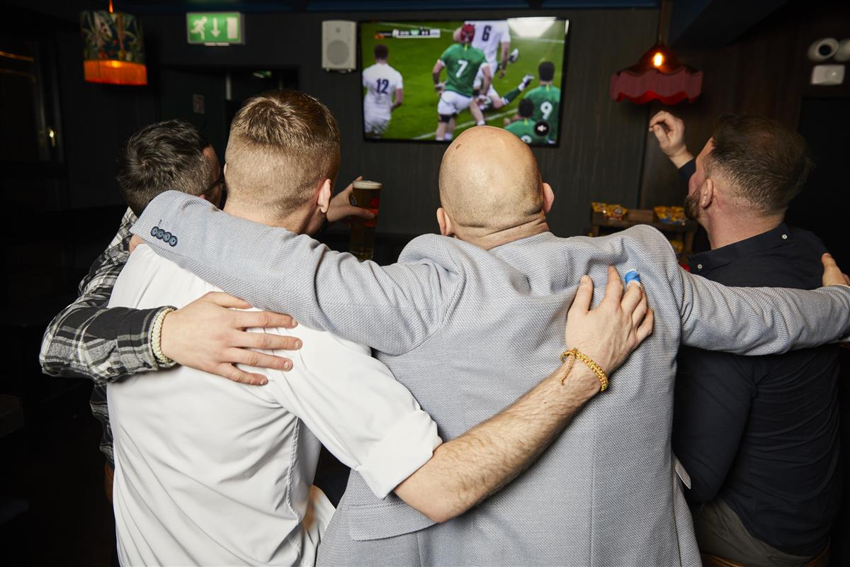 Lads with arms around shoulders watching the Irish National rugby team in action on the pitch on big screen TV at the Crown Quarter Wexford