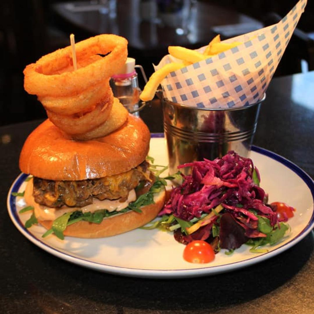 Burger with onion rings stacked on top and side salad at The Coach House in Gorey